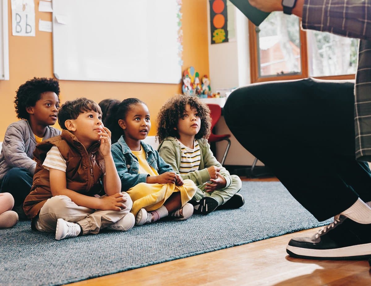 Young schoolchildren sitting on a classroom floor listening to their teacher